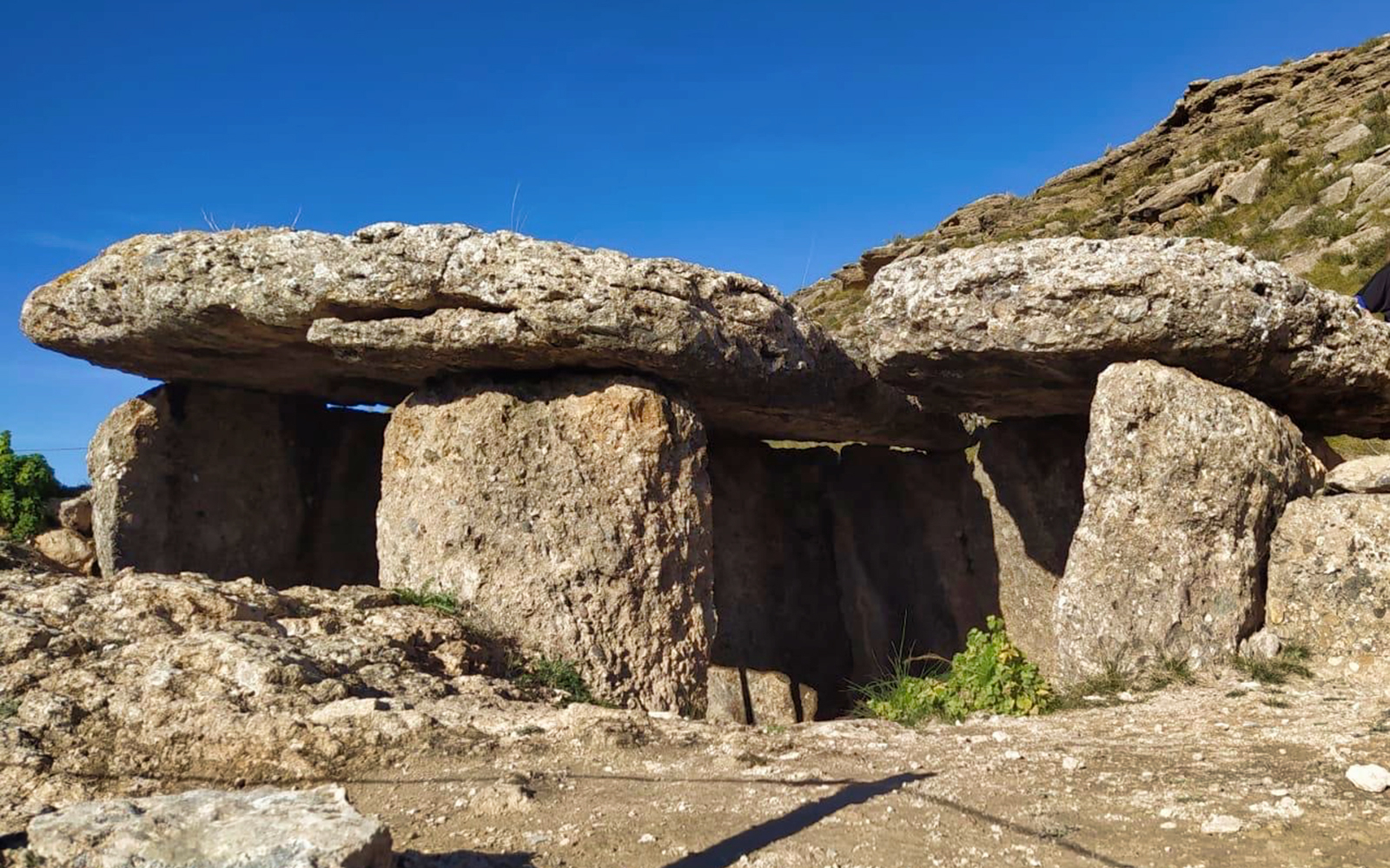 Ancient stone dolmen in Geopark Granada under a clear blue sky.