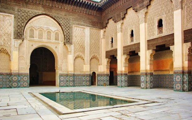 Courtyard of Ben Youssef Madrasa in Marrakesh with intricate tilework and central pool.