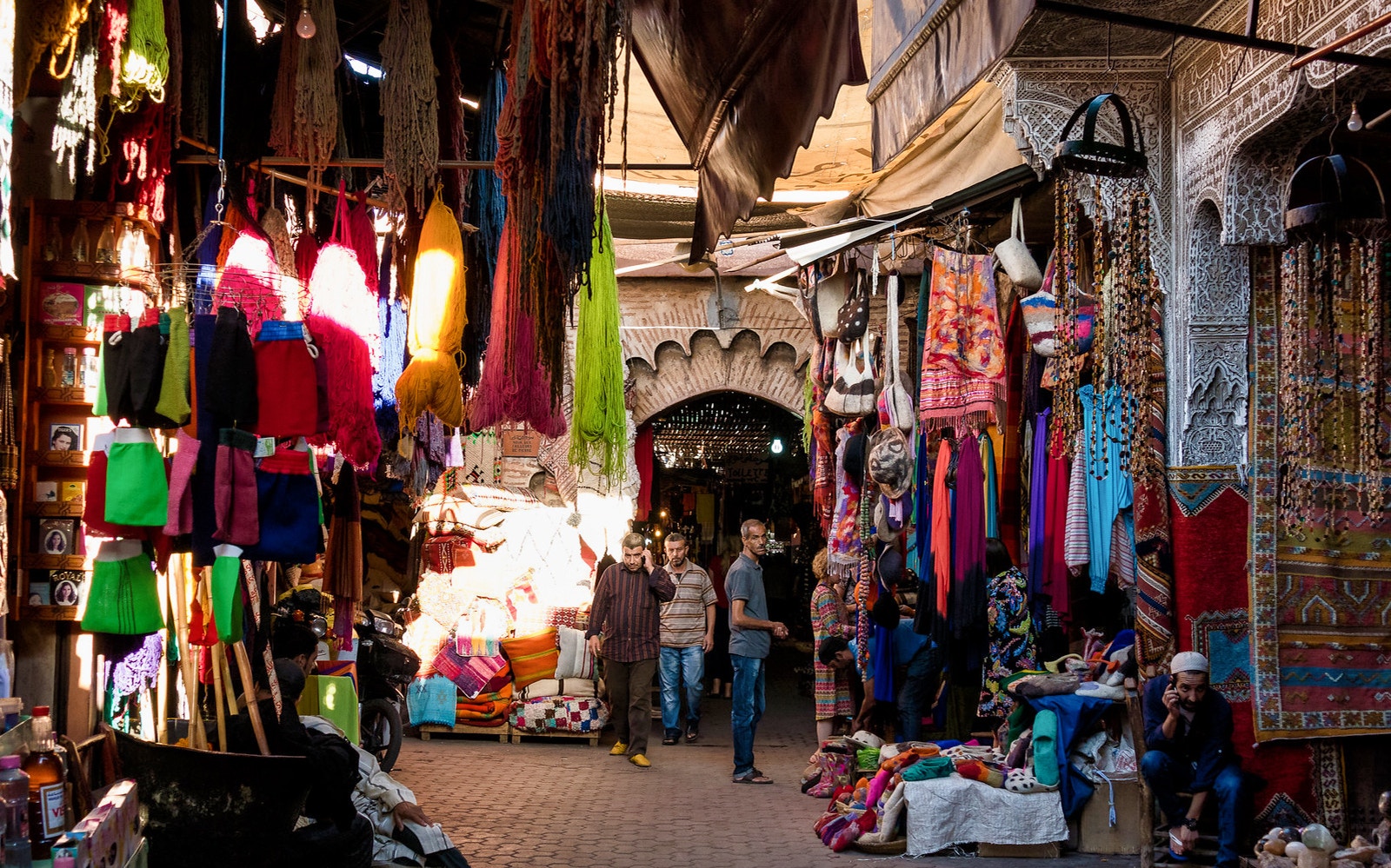 Marrakesh souk with colorful textiles and people walking through the Medina.
