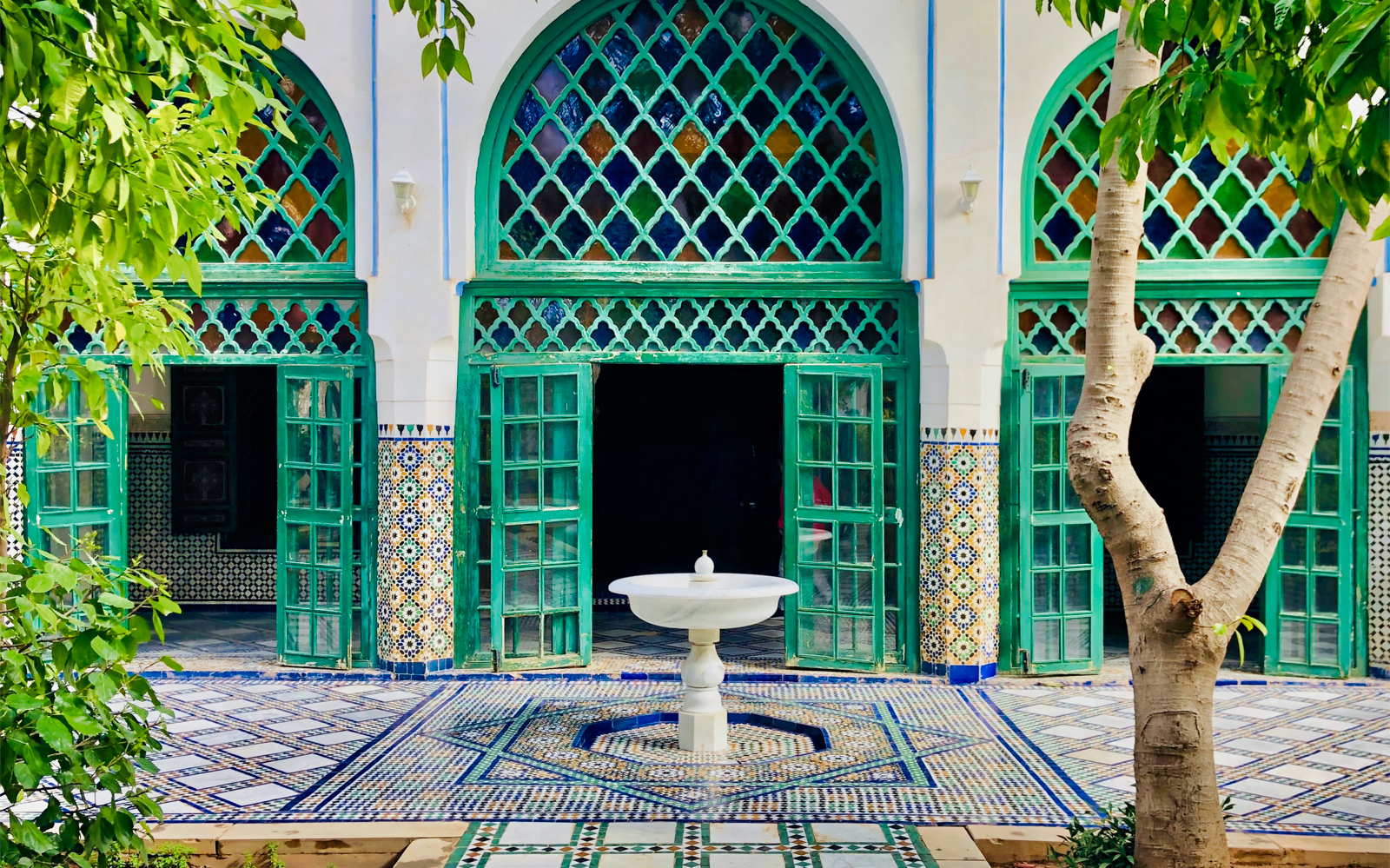 Bahia Palace courtyard with intricate tilework and green arched doors in Marrakesh.