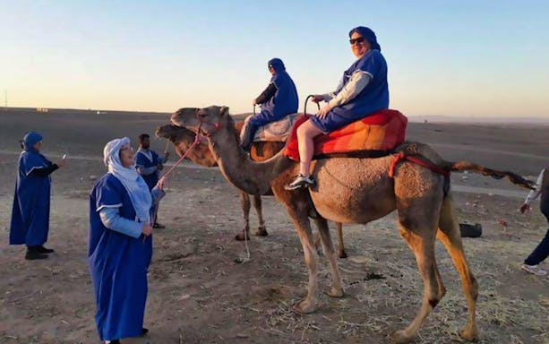 Camel ride in Agafay Desert with tourists in traditional attire, near Marrakesh.
