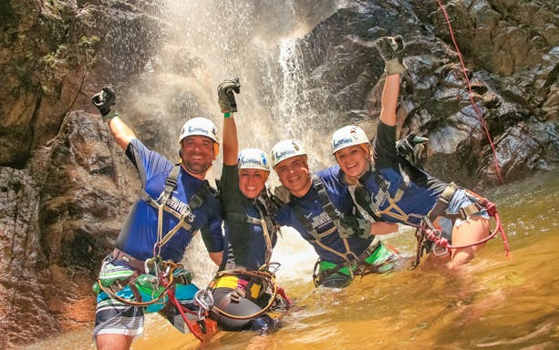 Adventurers in harnesses celebrate under a waterfall in Banderas Bay jungle.