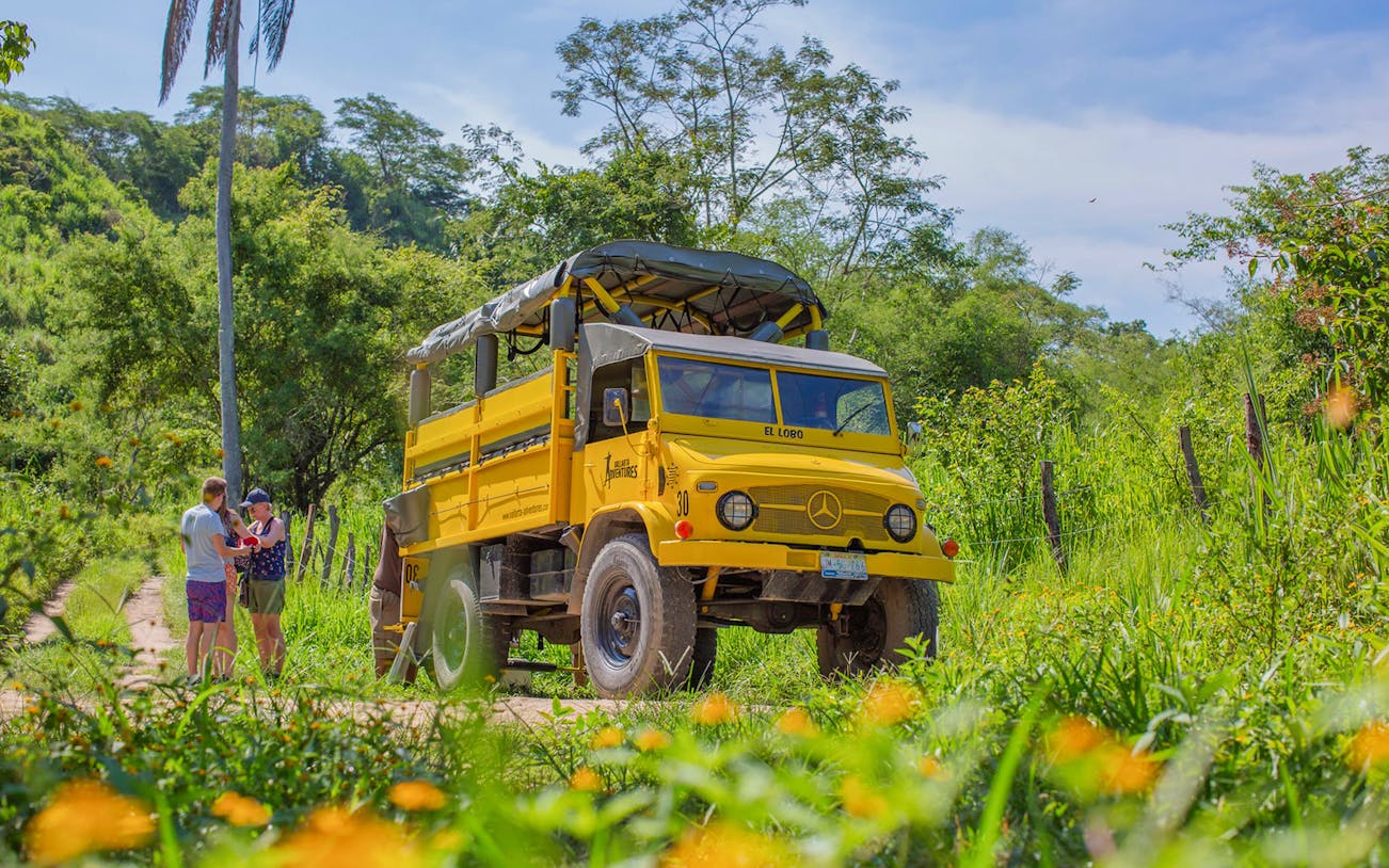Yellow truck on a jungle path in Banderas Bay with two people nearby.