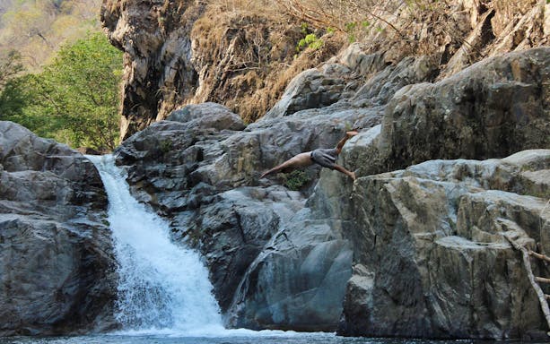 Man diving off rocks near waterfall at Jorullo Suspended Bridge ATV tour.