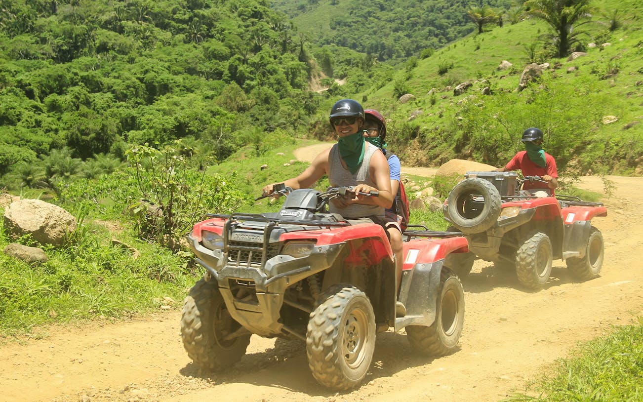ATV riders on Jorullo Suspended Bridge trail, lush greenery in background.