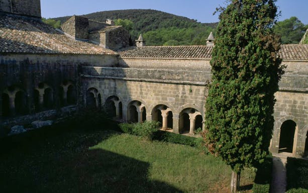 Cloister courtyard of Abbaye du Thoronet with stone arches and greenery.