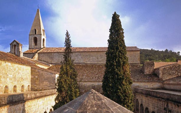 Abbaye du Thoronet with stone architecture and tall cypress trees in Provence, France.