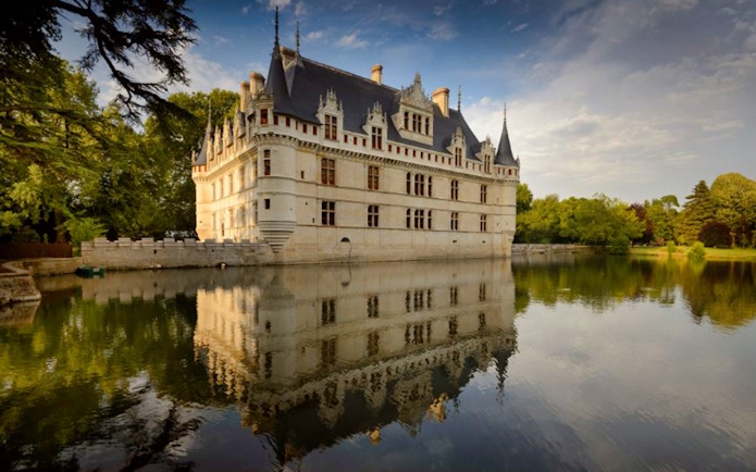 Azay le Rideau Castle reflecting in a calm moat, surrounded by lush greenery.