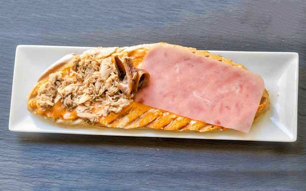 Open-faced sandwich with tuna, anchovies, and ham on a white plate, Almeria tapa tour.
