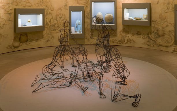 Wire sculptures in Almeria museum exhibit with ancient artifacts in background.