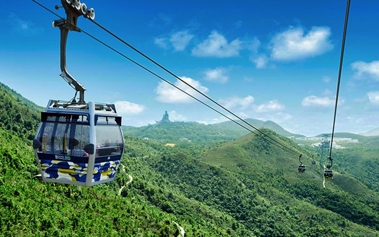 Cable car over lush hills with distant statue, part of 360 Sky Land Sea Day Pass (RoundTrip).