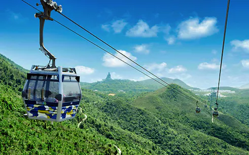 Cable car over lush hills with distant statue, part of 360 Sky Land Sea Day Pass (RoundTrip).