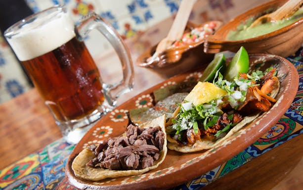 Tacos with meat and pineapple, lime wedges, and a mug of beer in Cancun.