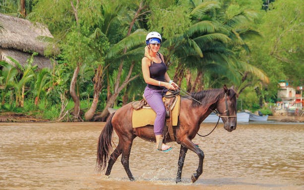 Horseback riding through a river in Banderas Bay, surrounded by lush greenery.