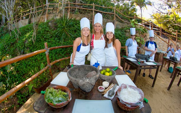 Cooking class at Las Caletas Beach with participants in chef hats and aprons, surrounded by ingredients.