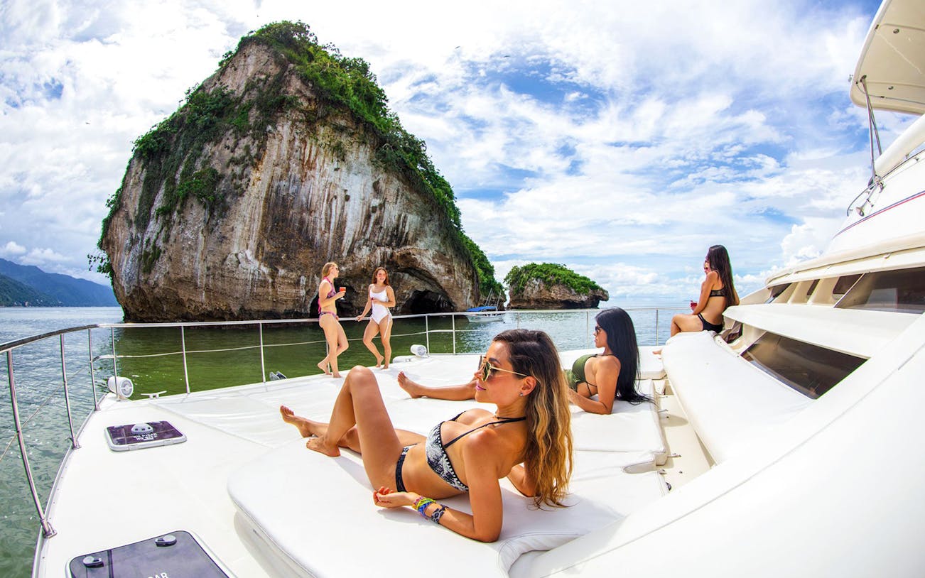 Luxury yacht with people relaxing near rock formations, Puerto Vallarta snorkeling tour.