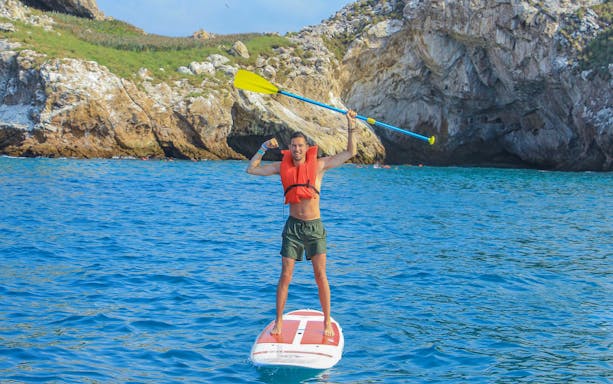 Paddleboarder in life vest near rocky cliffs at Islas Marietas, Puerto Vallarta.