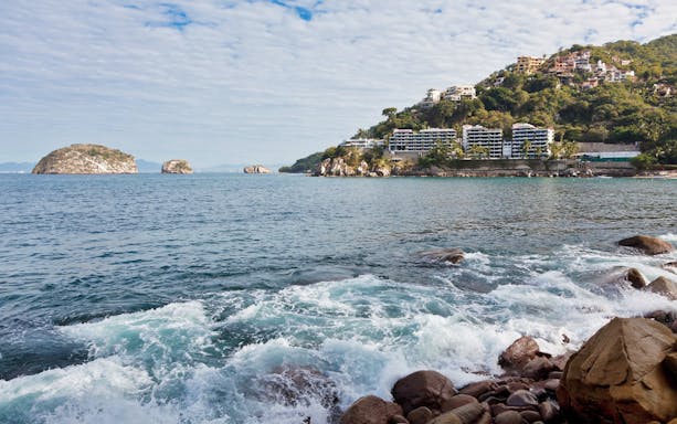 Coastal view of Sayulita Beach with rocky shoreline and hillside buildings, near Puerto Vallarta.