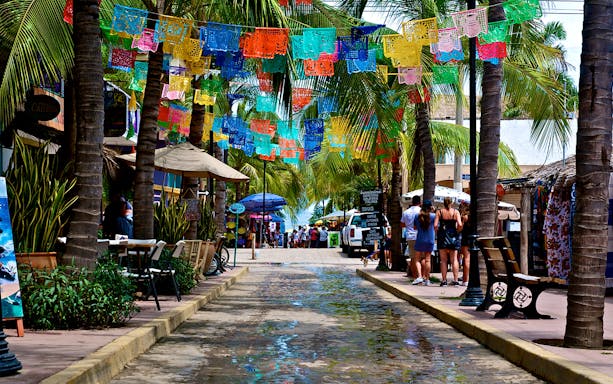 Colorful flags and palm trees line a vibrant street in Sayulita Beach Town, Mexico.
