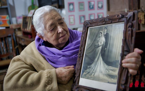 Elderly woman in San Sebastian holding a framed vintage wedding photo.