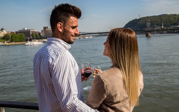 Couple enjoying drinks on a Danube River cruise in Budapest with cityscape in background.