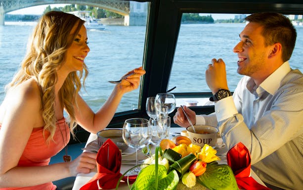 Couple dining on a Danube River cruise in Budapest with a view of the water and bridge.