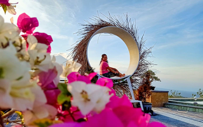 Person sitting in a circular swing with flowers in foreground during Bali sunrise tour.