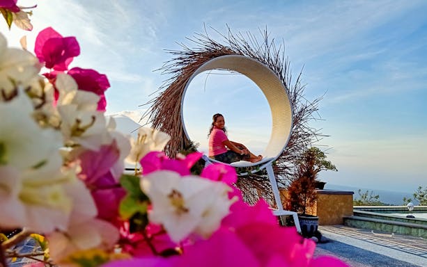 Person sitting in a circular swing with flowers in foreground during Bali sunrise tour.