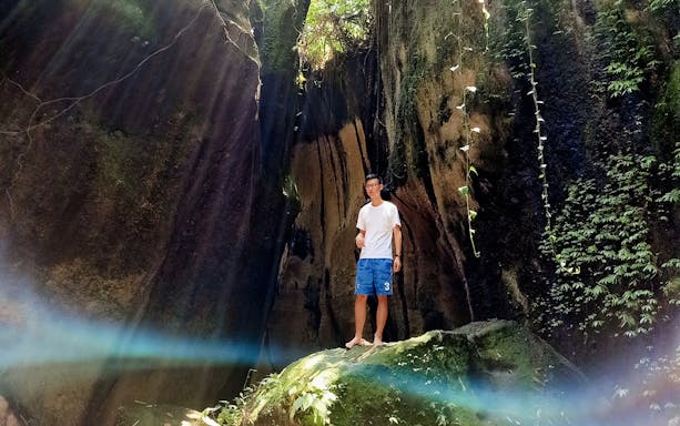 Man standing in a sunlit cave with lush greenery, Bali Instagram Private Tour.