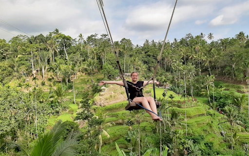 Person on a swing over lush rice terraces in Bali, Indonesia.