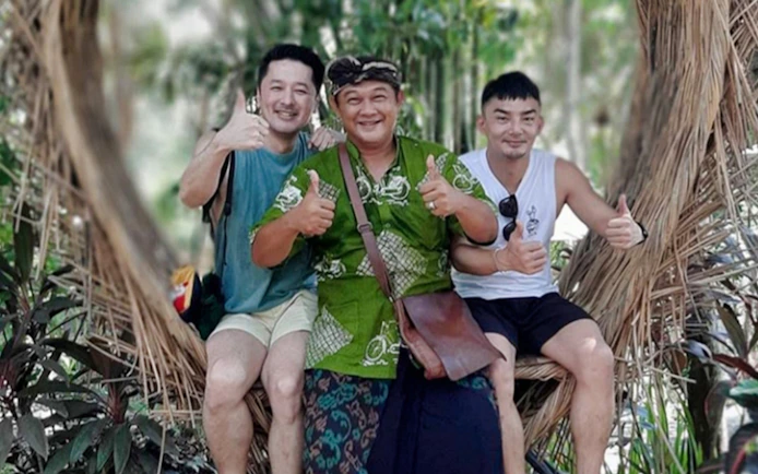 Tourists posing with a local guide in a scenic Bali jungle setting.