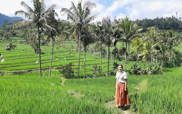 Person standing in Bali's lush Ubud rice terraces with palm trees in the background.