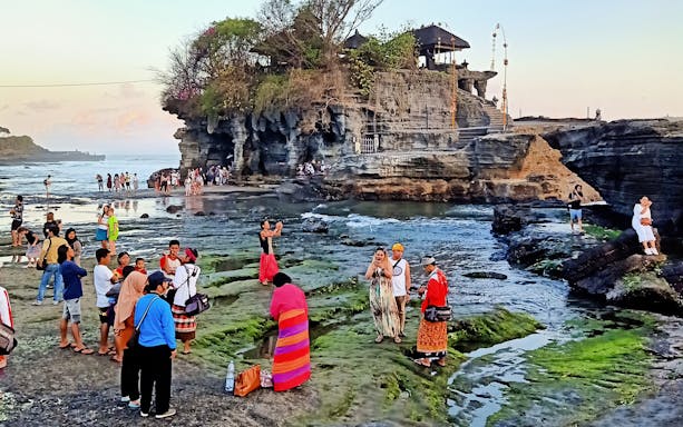 Visitors exploring Tanah Lot temple and rocky shoreline during Bali Private Bedugul, Tanah Lot Sunset Tour.