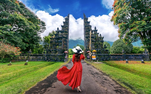 Woman in red dress walking towards Handara Gate in Bali, surrounded by lush greenery.