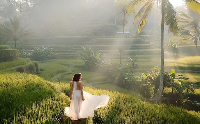 Woman walking through lush rice terraces in Ubud, Bali, with palm trees in the background.