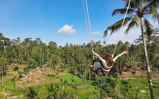Person swinging over rice terraces in Bali during a private tour.