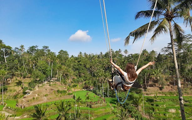 Person swinging over rice terraces in Bali during a private tour.