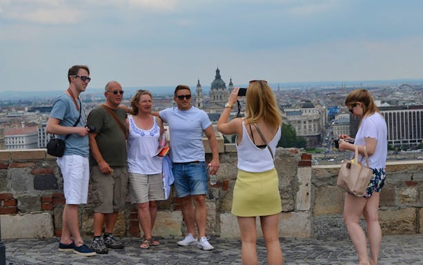 Tourists posing for a photo on Gellért Hill with Budapest skyline in the background.