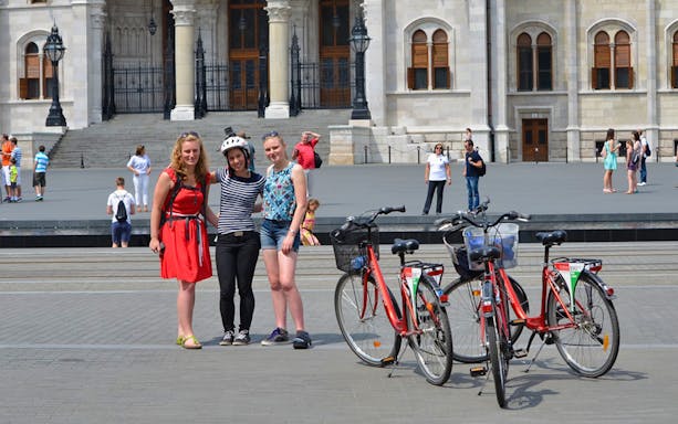 Group of tourists with bikes in front of Budapest Parliament during city tour.