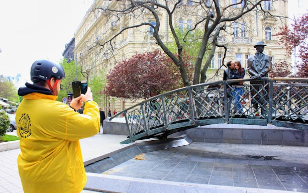 Tourist photographing a couple on a bridge with a statue in Budapest during a Segway tour.