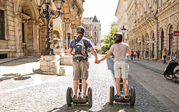 Two people on Segways holding hands on a cobblestone street in Budapest.