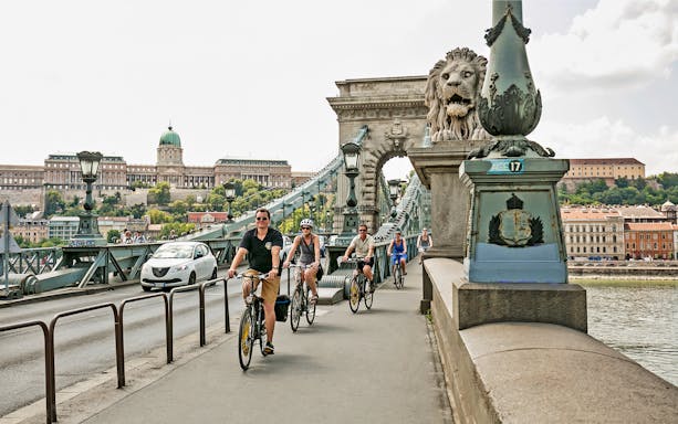 Cyclists on Chain Bridge with Buda Castle in view, Budapest Danube River bike ride.