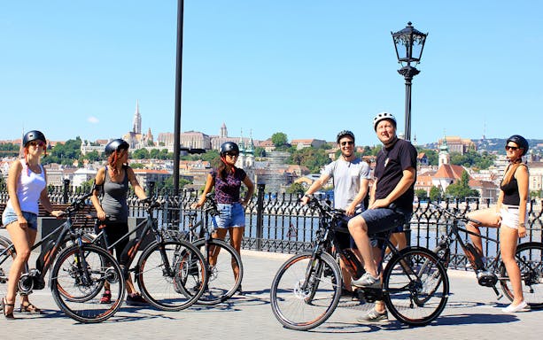 Group on e-bikes with Budapest skyline in the background during city tour.