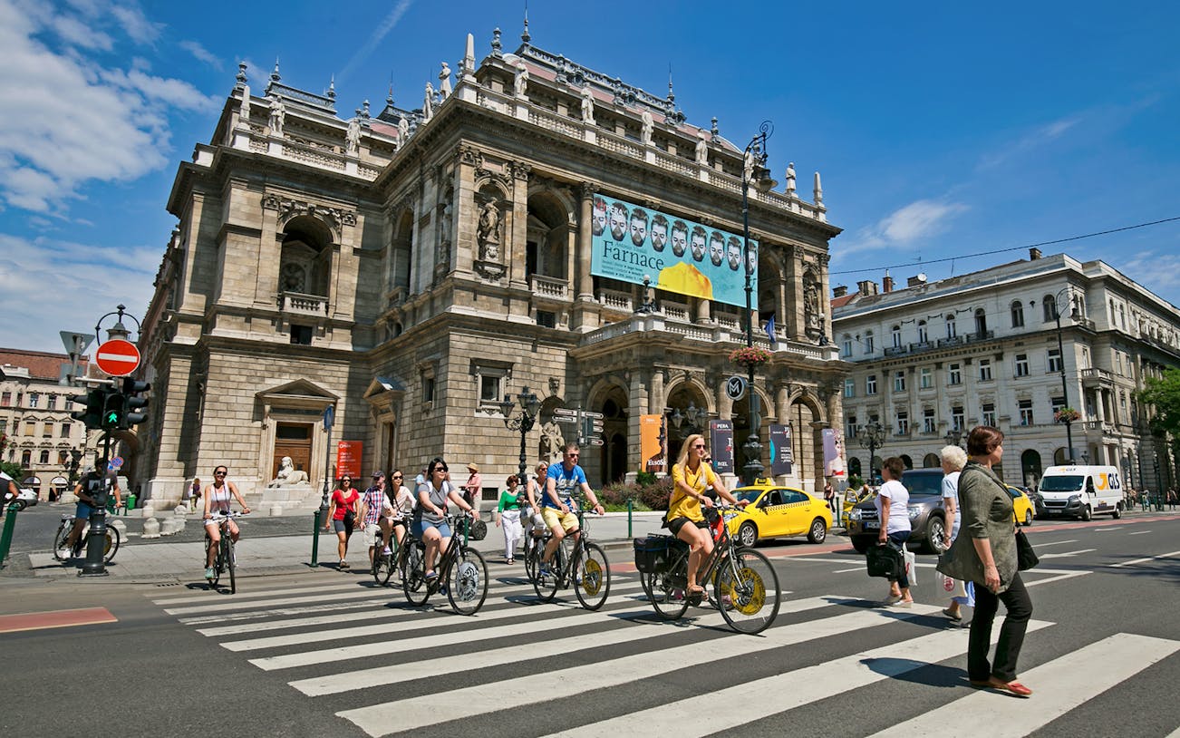 Cyclists on e-bikes crossing in front of the Hungarian State Opera House, Budapest.