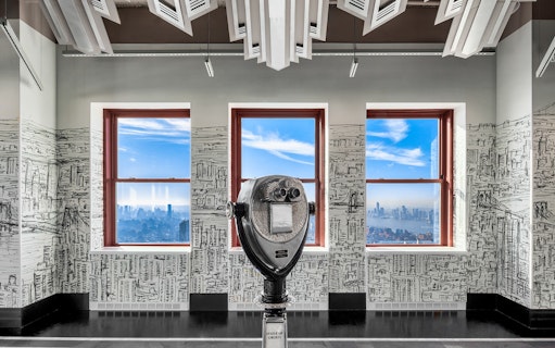 Observation deck view of New York City skyline through windows with a coin-operated viewer.