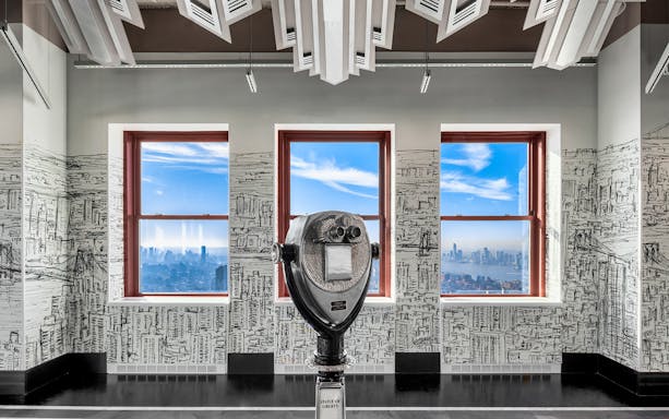 Observation deck view of New York City skyline through windows with a coin-operated viewer.