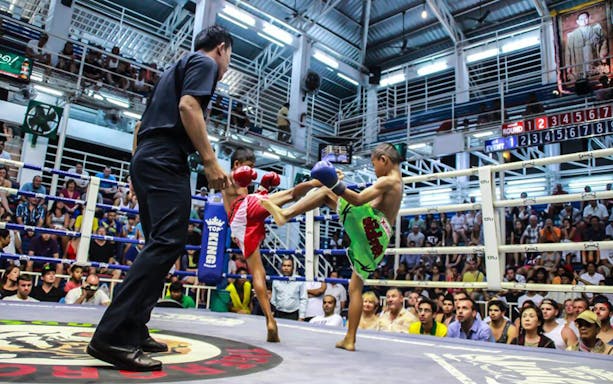 Muay Thai match at Bangla Boxing Stadium, Phuket, with a referee and audience watching.