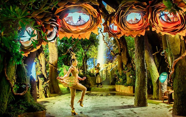 Dancer in elaborate costume performing in forest setting at Tribhum Adventure Park.
