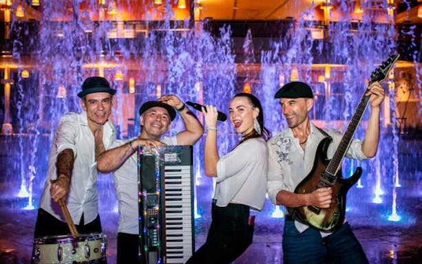 Musicians performing at Blue Tree Water Park with colorful fountains in the background.