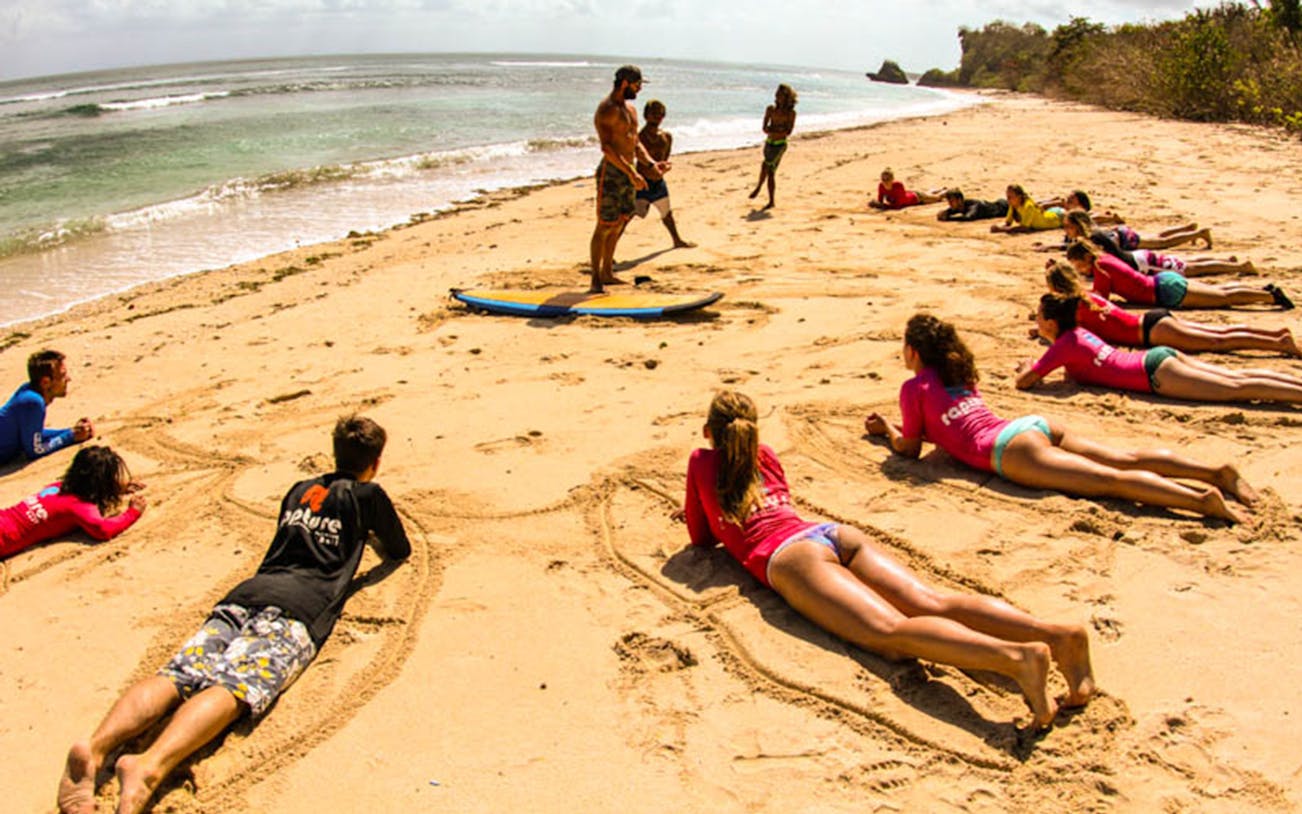 Surf instructor teaching a group on a Bali beach, practicing on sand before hitting the waves.